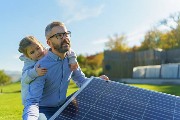 istock Father with his little daughter catching sun at solar panel,charging at their backyard. Alternative energy, saving resources and sustainable lifestyle concept. 1437508297
