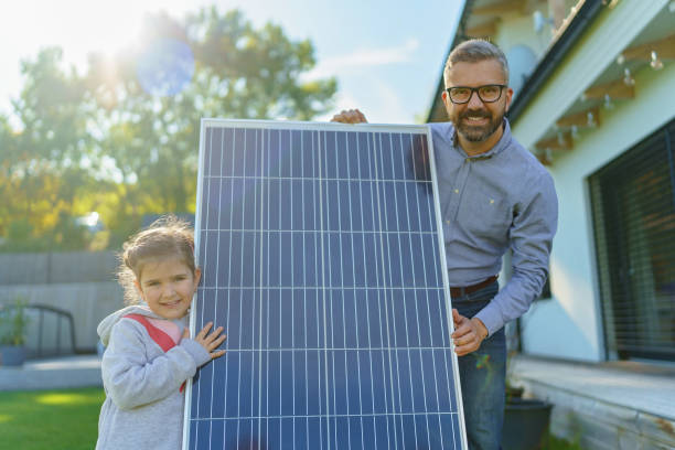 Father with his little daughter near their house with solar panels. Alternative energy, saving resources and sustainable lifestyle concept. stock photo
