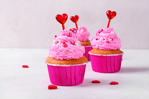 Cupcake with pink icing decorated with sugar sprinkles and heart toppers. Serving size dessert for Valentine's Day