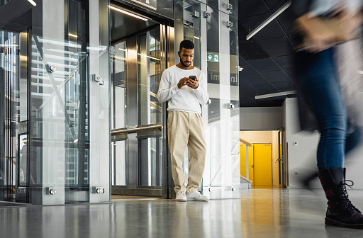 Young man exiting the elevator, using phone