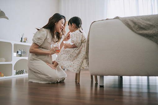 Chinese pregnant mother enjoying orange juice with her daughter in living room