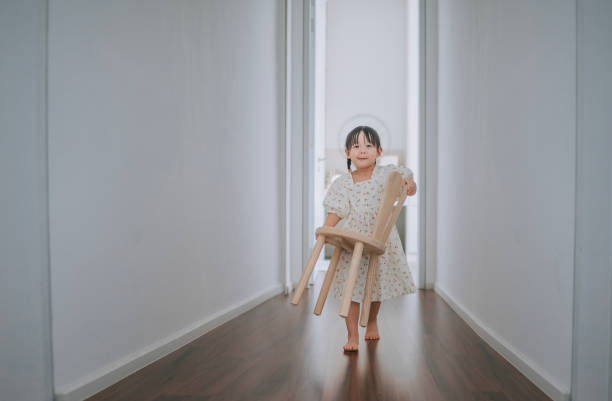 ragazza cinese asiatica che trasporta la sedia di legno che cammina verso la macchina fotografica a casa - two girls only cheerful front view horizontal foto e immagini stock