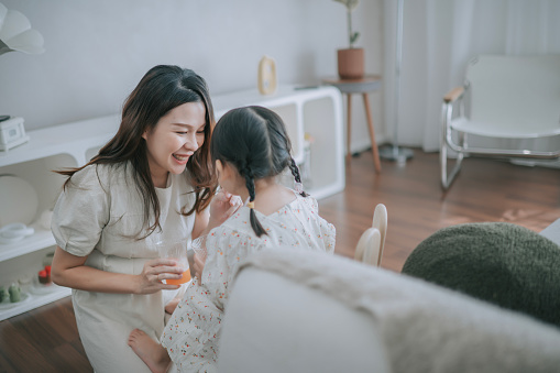 Chinese pregnant mother enjoying orange juice with her daughter in living room