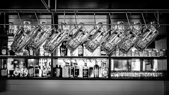 A black and white shot of glass beer cups hanging in a bar