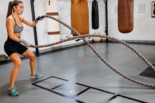 Fitness woman using training ropes for exercise at gym. Athlete working out with battle ropes at gym.