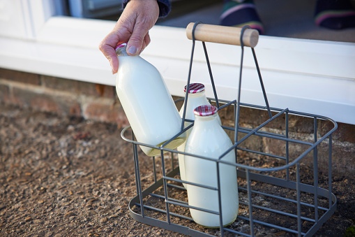 Person Picking Up Bottle Of Milk From House Door Step