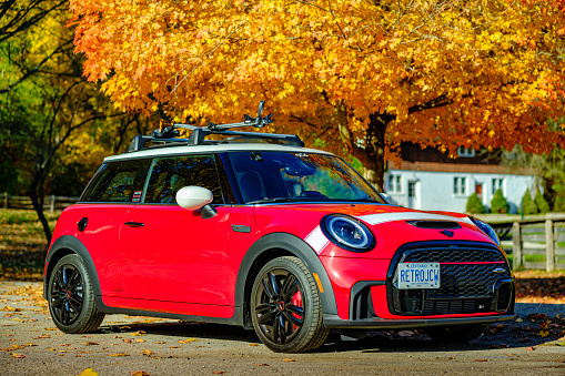 Toronto, Ontario, Canada- October 29, 2022. Chili red colour MINI COOPER on the road in public park against fall nature colours in Toronto East side, Canada. This is the third generation model F56 JCW, since BMW took over iconic brand of MINI. MINI featured in the photo is John Cooper Works model, the most powerful 2 door version. For the first time, this compact car features engine build and designed by BMW, and packs even more power and torque than previous models since 2002 to present. Original design clues and themes are still present on this brand new model. Mini has been around since 1959 and has been owned and issued by various car manufacturers.