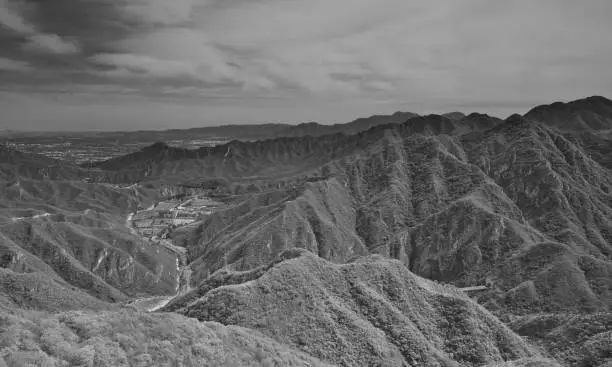 Photo of View of historical Great Wall surrounded by forested mountains in China under cloudy sky. Grayscale