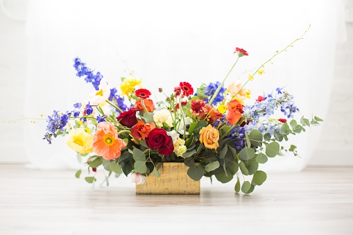A horizontal shot of a bouquet full of different colored flowers in a square basket in front of a white background