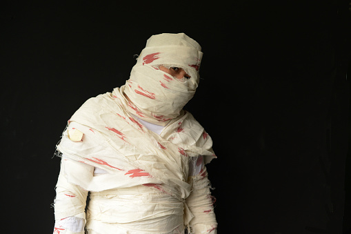 Bandaged mummy in standing position with black background on Halloween day.
