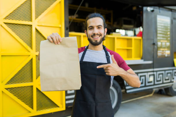 Smiling cook holding a mock up delivery bag with street food stock photo