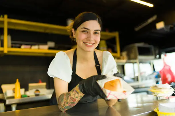 Beautiful smiling woman working as a cook and serving a sandwich at the food truck