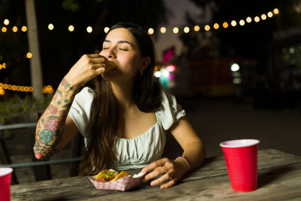 Hungry mexican woman eating delicious tacos Attractive hispanic woman looking hungry enjoying eating delicious mexican tacos from the food truck at night evening meal stock pictures, royalty-free photos & images