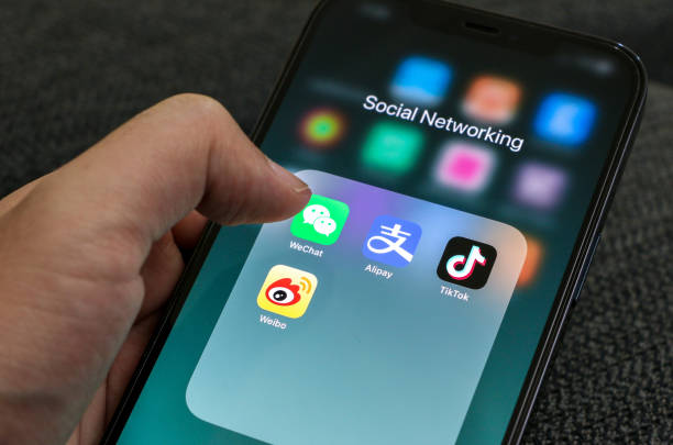 親指でスマートフォンを持ち、wechatアイコンをクリックし、アリペイ、ティックトック、weiboのアイコンとともに画面に表示されます。ソーシャルメディアのコンセプト。 - twitter iphone apple computers application software ストックフォトと画像