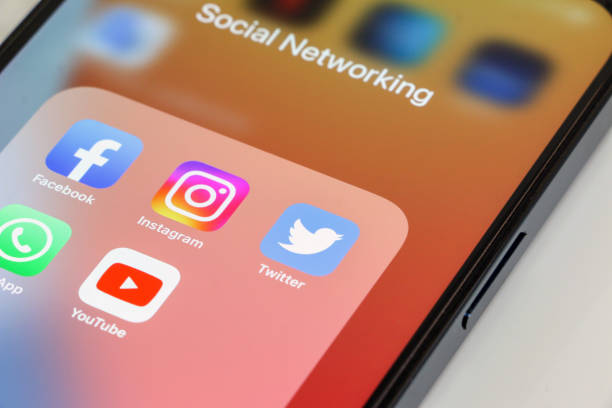 primer plano de los iconos de aplicaciones populares de redes sociales, facebook, instagram, twitter, whatsapp y youtube, en ese orden, que se muestran en la pantalla del teléfono inteligente con fondo de pantalla naranja. el dispositivo está sobre fondo - facebook twitter iphone social networking fotografías e imágenes de stock