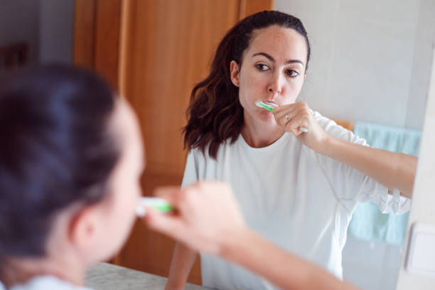 istock Smiling young woman brushing teeth in bathroom. Happy girl looking in mirror while using ecological toothbrush with whitening toothpaste. 1437530477