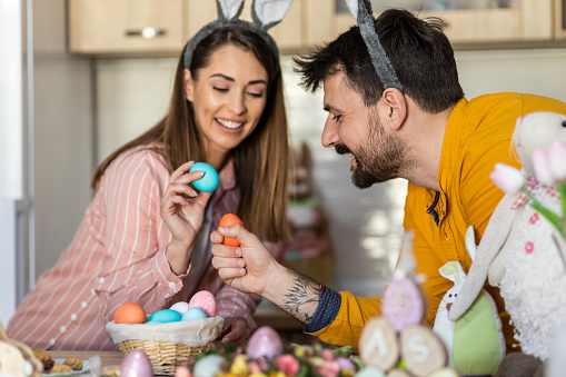 Portrait of a beautiful young newlywed couple smiling and goofing around with Easter decoration, celebrating Easter at home. Happy family celebrating Easter. Happy Easter. Easter background image. Easter eggs. Easter 2023.