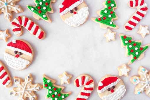Cute Christmas cookie frame. Top down view on a white marble background with copy space. Holiday baking concept. Santa Claus, tree, snowflakes, candy canes, stars.