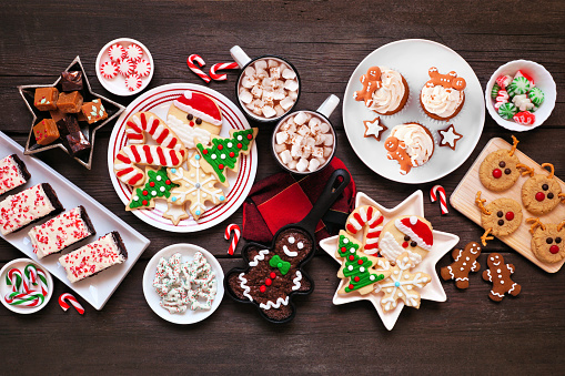 Cute Christmas sweets and cookie table scene. Top down view on a rustic dark wood background. Fun holiday baking concept.