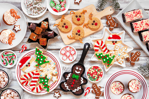 Overhead view of a white background filled with ingredients for preparing Christmas cookies. A cooling rack and a baking sheet with fresh baked cookies complete the composition. High resolution 42Mp studio digital capture taken with SONY A7rII and Zeiss Batis 40mm F2.0 CF lens