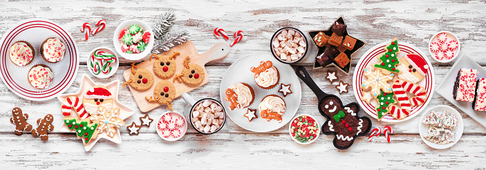 Cute Christmas sweets and cookie table scene. Overhead view on a rustic white wood banner background. Fun holiday baking concept.