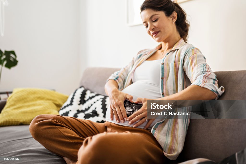 Smiling pregnant woman holds hands in heart shape A pregnant woman holds an ultrasound image 20-29 Years Stock Photo