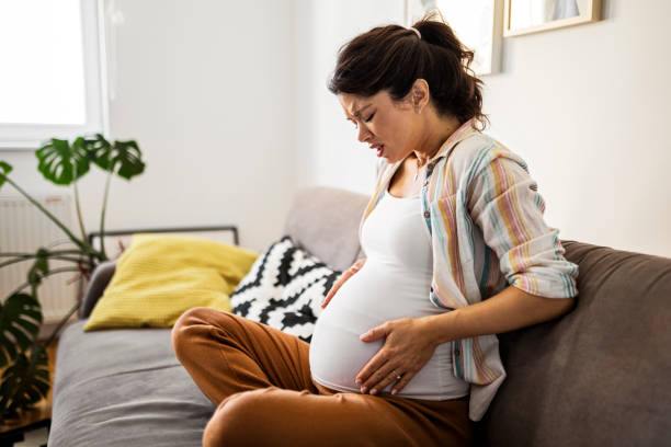 Pregnant young woman grimacing with hands on stomach Pregnant young woman grimacing with hands on stomach while sitting at home muscular contraction stock pictures, royalty-free photos & images