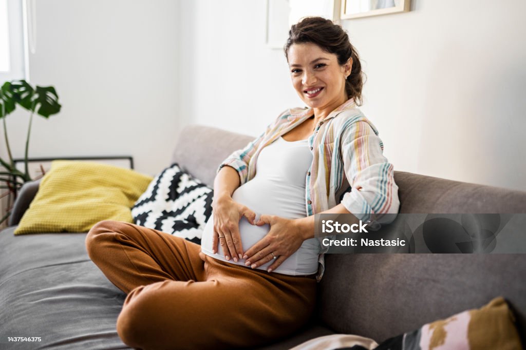 Smiling pregnant woman holds heart shape with hands on pregnant belly A pregnant woman holds an ultrasound image 20-29 Years Stock Photo
