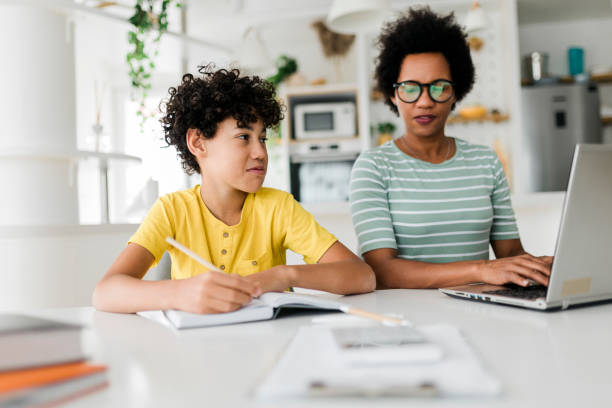 istock Boy writing on a book while his mother working on laptop. Kid studying with mother working from home. 1437552525