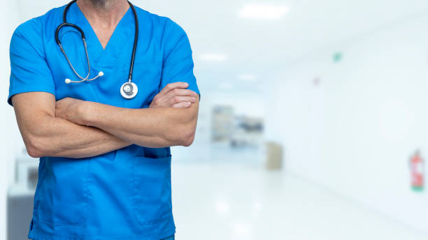 médico cirurgião ou enfermeiro em esfregões azuis com braços cruzados e estetoscópio no corredor do hospital. conceito de plano de saúde e seguro de saúde. - male nurse medical student healthcare and medicine nursing assistant - fotografias e filmes do acervo