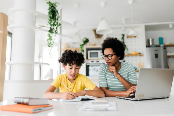 istock Boy writing on a book while his mother working on laptop. Kid studying with mother working from home. 1437555570