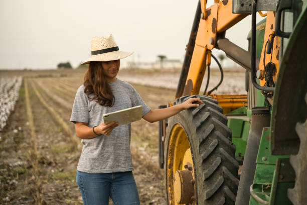 portret uśmiechniętej młodej rolniczki używającej tabletu i traktora do zbiorów. nowoczesne rolnictwo z koncepcją technologii i maszyn - business agriculture equipment farm zdjęcia i obrazy z banku zdjęć