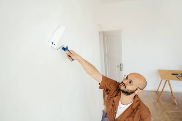 istock Smiling young man painting wall with paint roller 1437559498