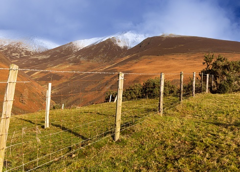 A wooden fence wrapped with barbed wire in the field with mountains in the background