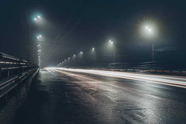route brumeuse brumeuse de nuit illuminée par des lumières de rue - night wet road street photos et images de collection
