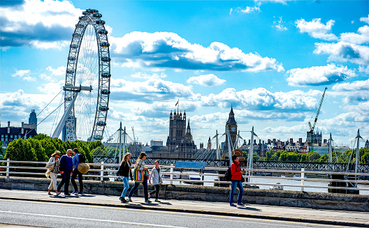 Tourist walking along the South Bank of the Thames in London, England with The London Eye, Big Ben, and Parliament in the background.  All three are very popular tourists attractions in London.