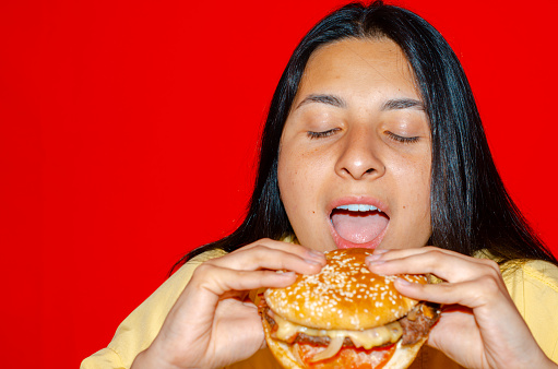 Woman eating a hamburger with red background