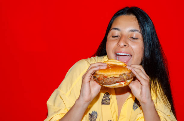 istock Woman eating a hamburger with red background 1437567078