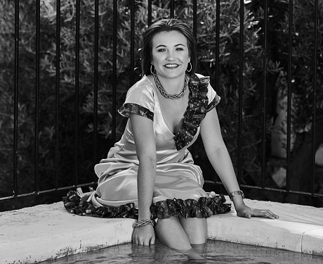 A grayscale portrait of a smiling woman sitting by a pool