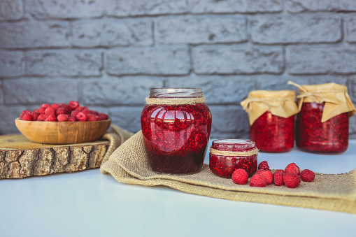 Glass jar with delicious homemade raspberry jam on table.