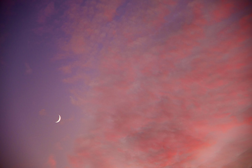 A sliver of a Moon in the left corner surrounded by clouds.