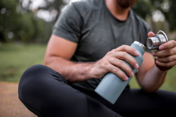 Close up of a reusable water bottle in a human hand, concept of thirst, rehydration and decreasing single use plastic Close up of a reusable water bottle in a human hand, concept of thirst, rehydration and decreasing single use plastic flask stock pictures, royalty-free photos & images