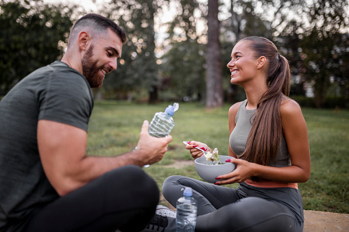 Happy sporty couple eating vegetable salad and drinking water after intensive workout