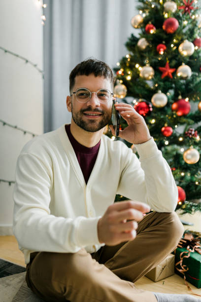 istock Young man sitting by Christmas tree and using his smart phone 1437581060