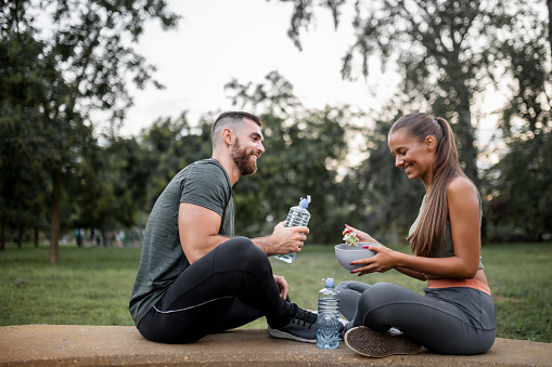 Happy sporty couple eating vegetable salad and drinking water after intensive workout
