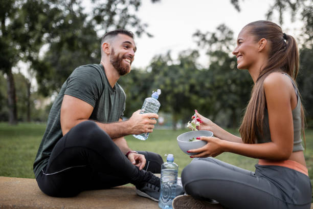 glückliches sportliches paar beim essen von gemüsesalat und trinkwasser nach intensivem training - eating body building muscular build vegetable stock-fotos und bilder