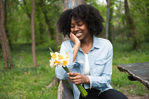 Portrait of a beautiful, young African American woman carrying a flower bouquet and enjoying in the park