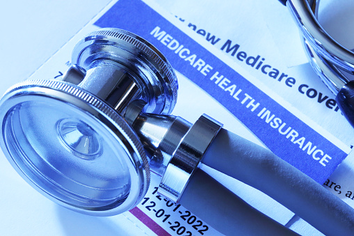 A stethoscope rests on top of a US government Medicare Health Insurance membership card. Photographed in a studio setting.