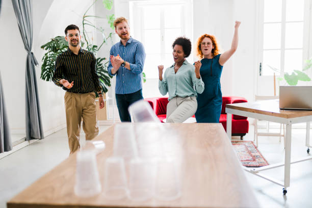 istock Business people having fun at the office, playing office games while on a break, tearing down a pyramid of plastic cups with a  ball 1437588325