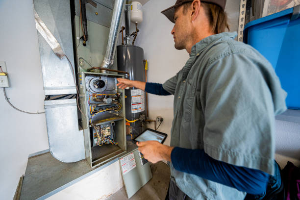 Young Male Property Inspector Photographing a Furnace Hot Water Heater and Air Conditioning Unit Inside a Residential Home Garage stock photo
